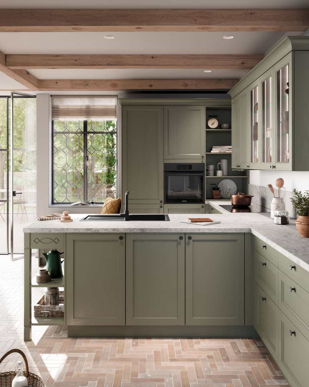 Cuisine équipée traditionnelle vert sauge avec îlot central et plan de travail en pierre naturelle, vitrines et sol en chevrons. IDEO cuisines sur mesure